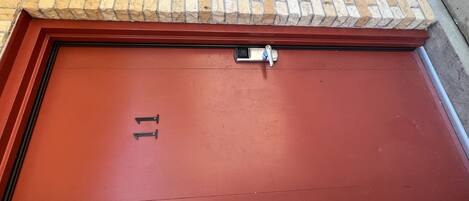 Una puerta roja con el número 11, un teclado de seguridad y una pequeña ventana encima.