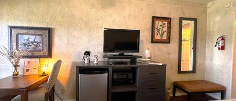 Quarto de hotel com cama, escrivaninha com televisão, máquina de café e quadro na parede.