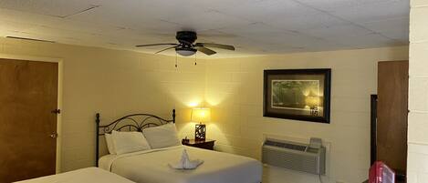 A hotel room with two beds, a ceiling fan, a framed picture on the wall, and a nightstand with a lamp.