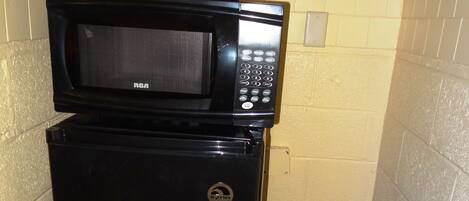 A compact kitchenette with a black refrigerator, a microwave, and a coffee maker.