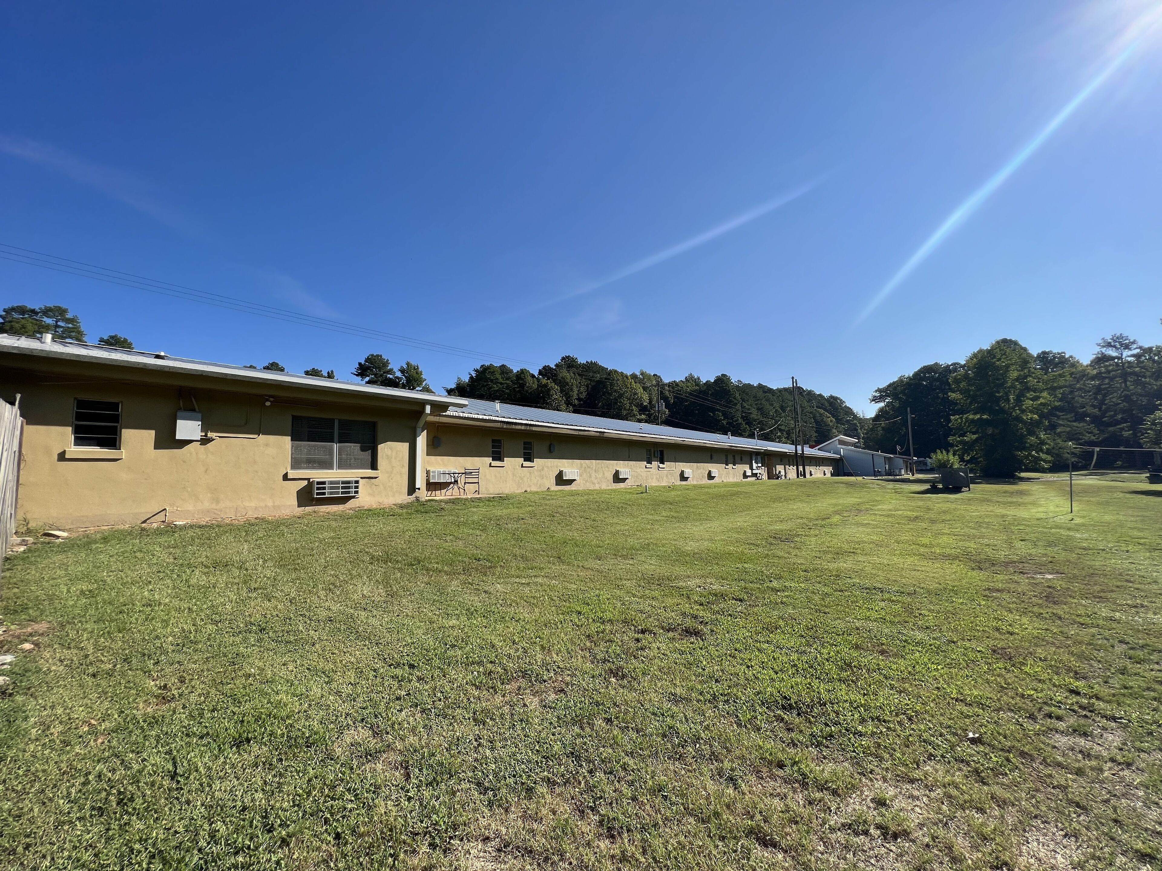 A row of single-story buildings with a flat roof and a grassy field in front.