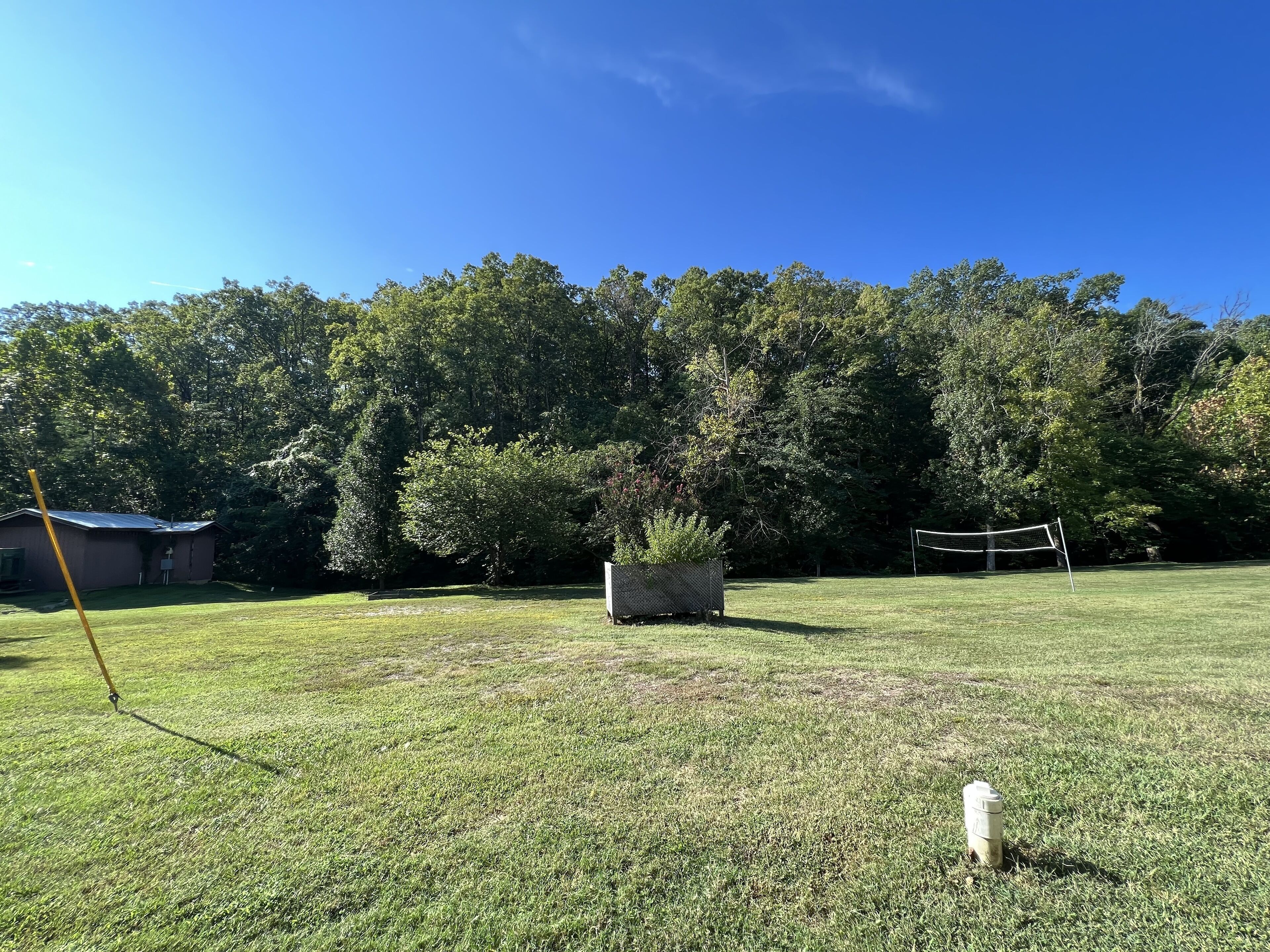 A grassy field with a volleyball net, a shed, and a planter box.