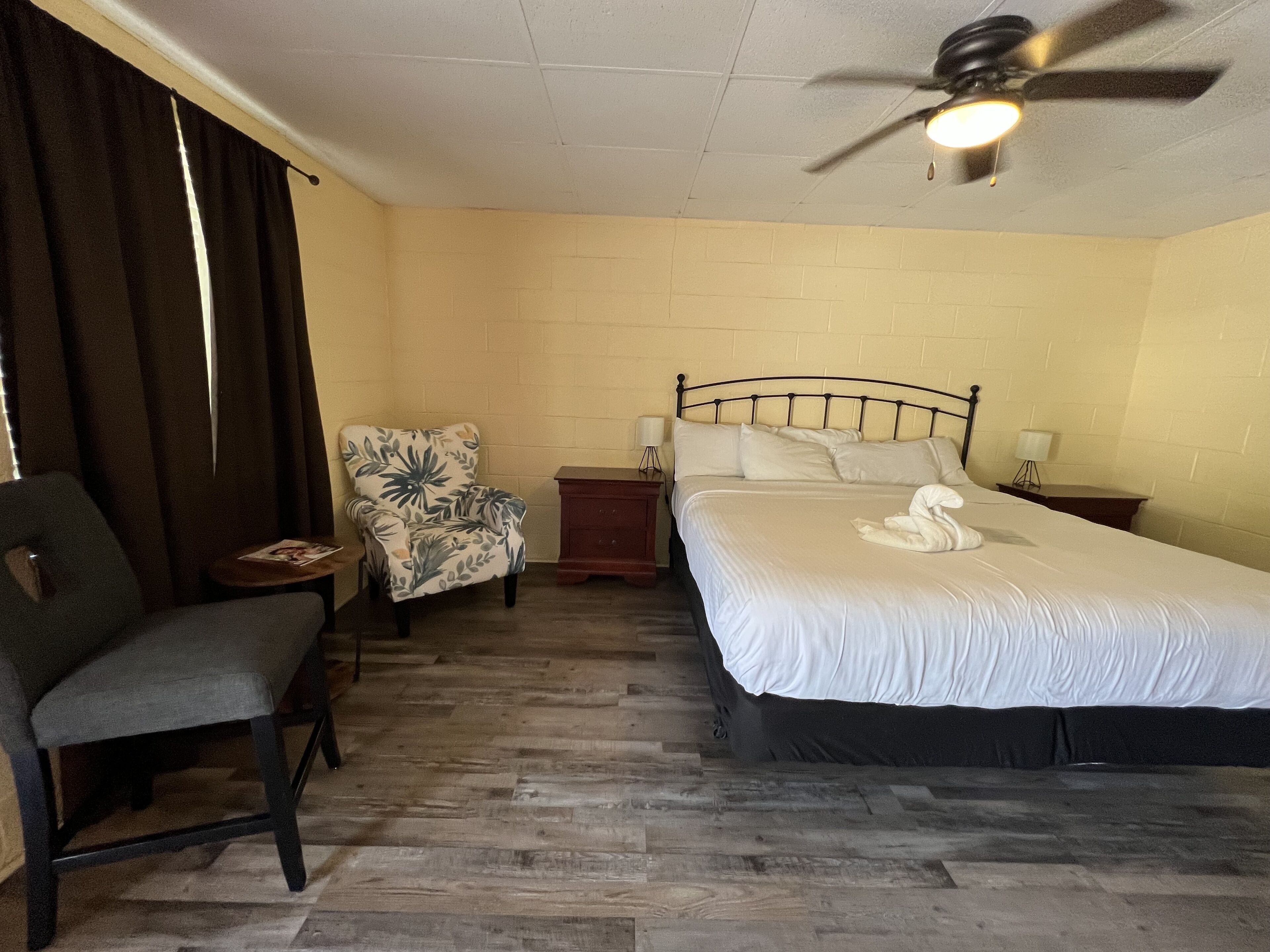 A hotel room with a bed, a chair, a nightstand, a lamp, and a ceiling fan.