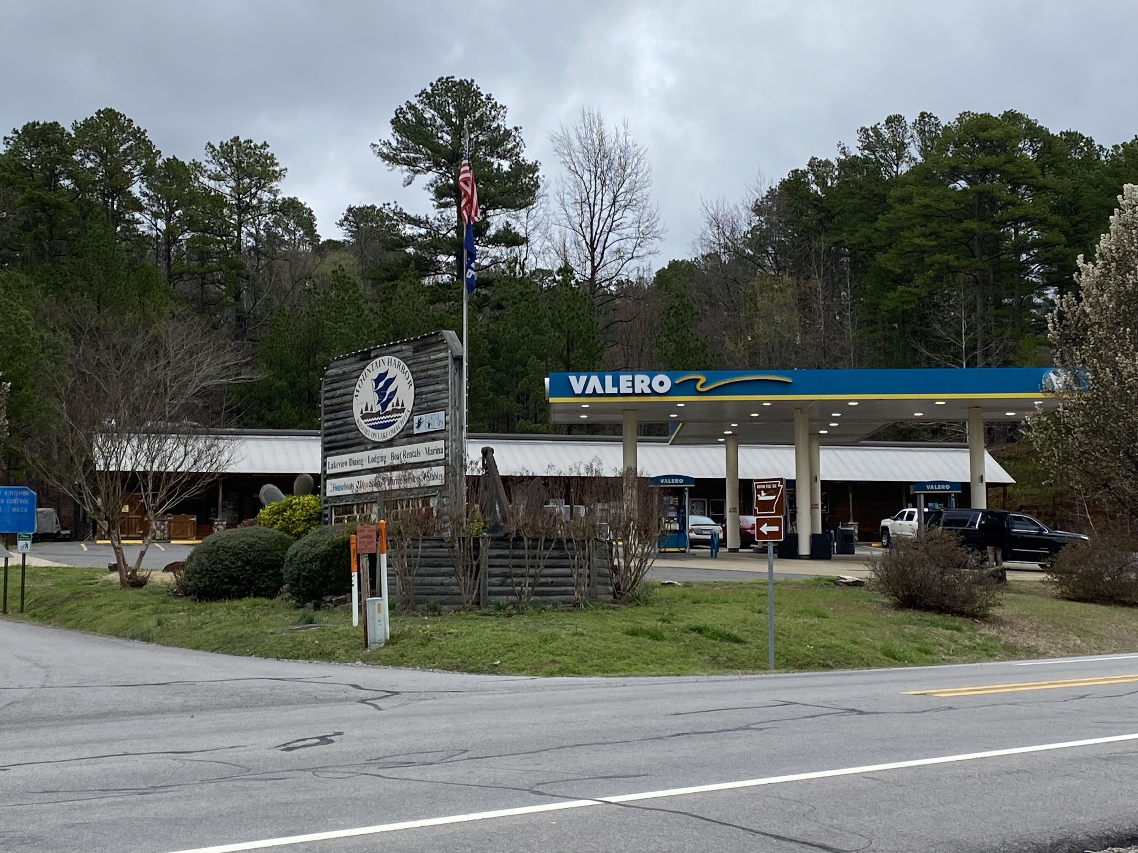 Una estación de servicio con un letrero de Valero, un cartel de madera que indica Mountain Harbor y una antena parabólica.