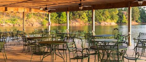 An outdoor patio with tables and chairs, overlooking a body of water.