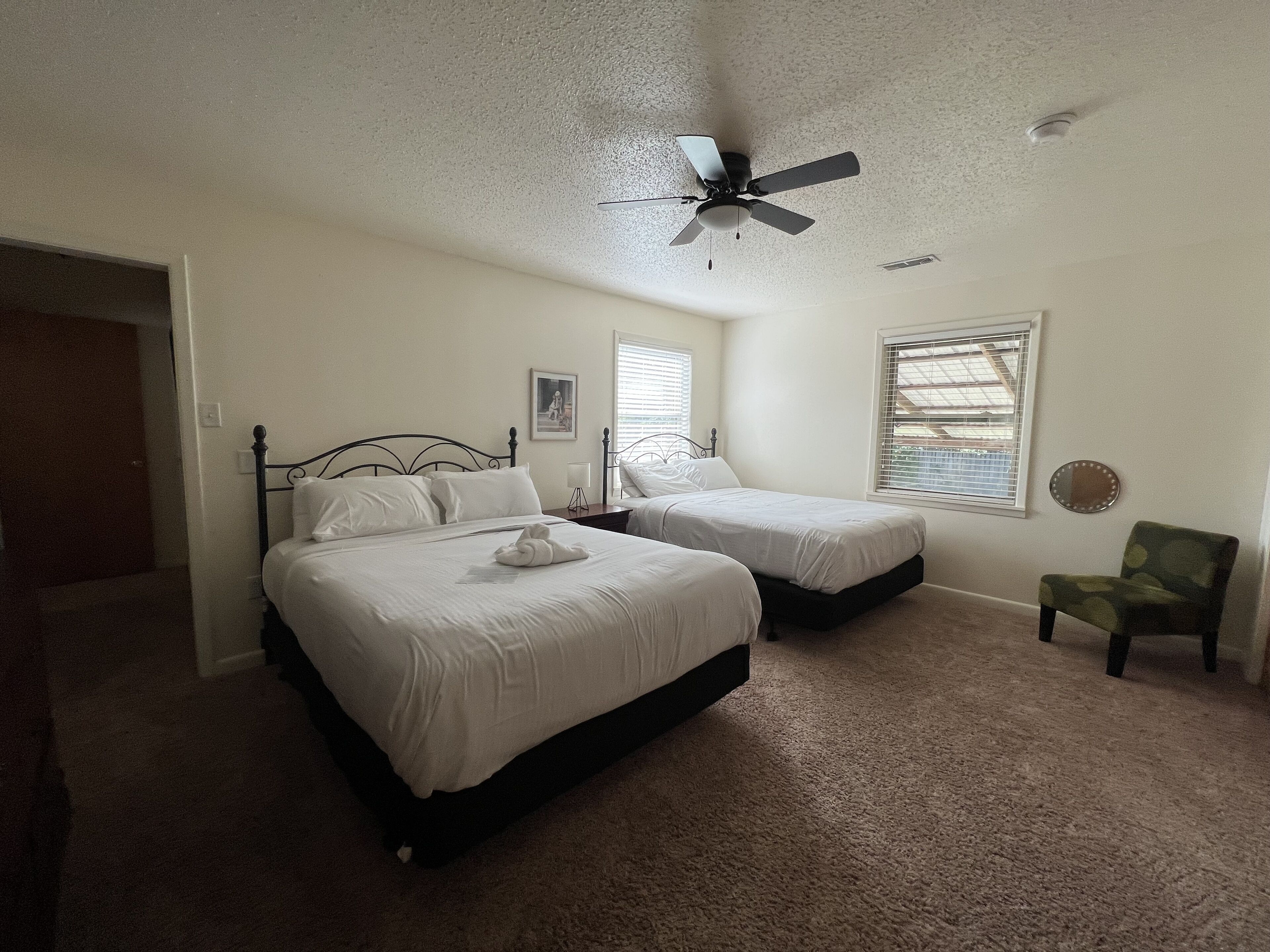 A bedroom with two beds, a ceiling fan, a chair, and a window with blinds.