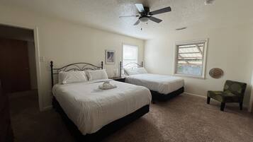 A bedroom with two beds, a ceiling fan, a chair, and a window with blinds.