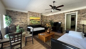 Une chambre d’hôtel avec un mur en briques, un lit, un bureau, une chaise, une télévision et un ventilateur de plafond.
