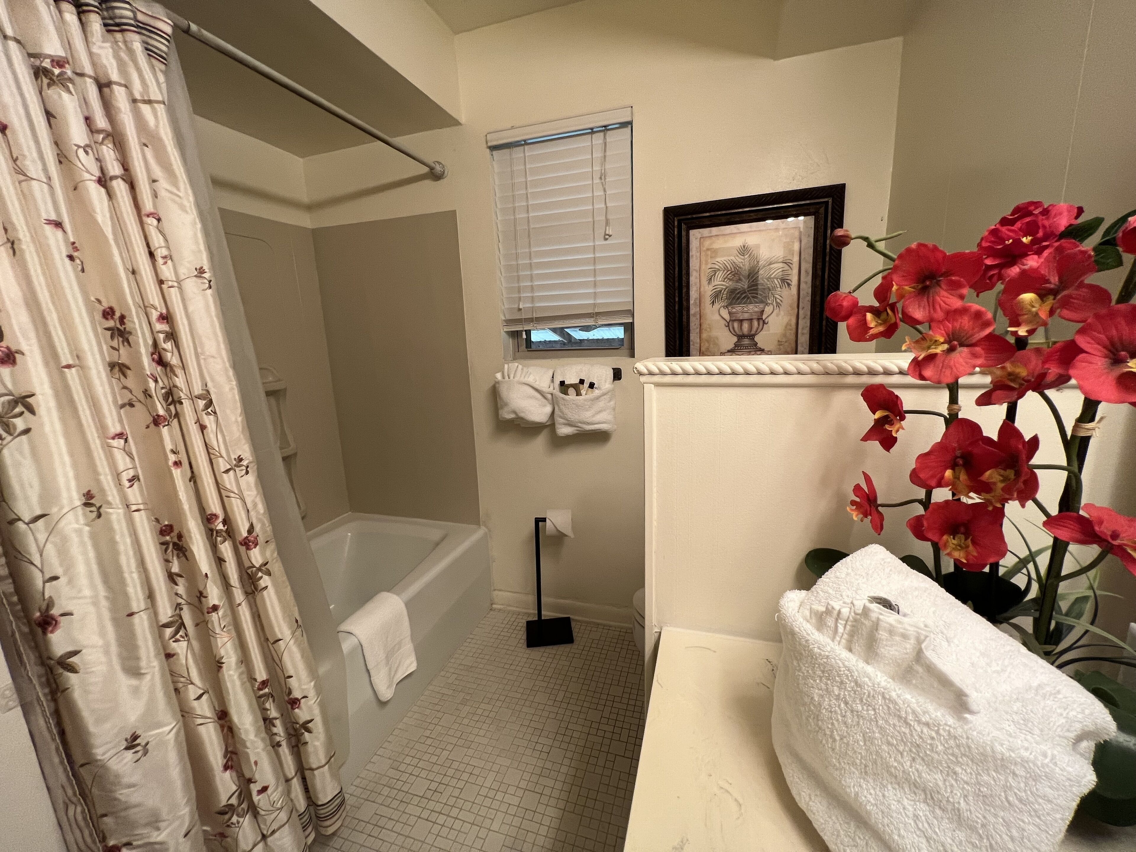 A bathroom with a bathtub, shower curtain, towel rack, window, and a potted plant.