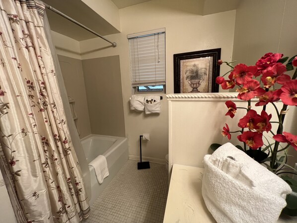 A bathroom with a bathtub, shower curtain, towel rack, window, and a potted plant.