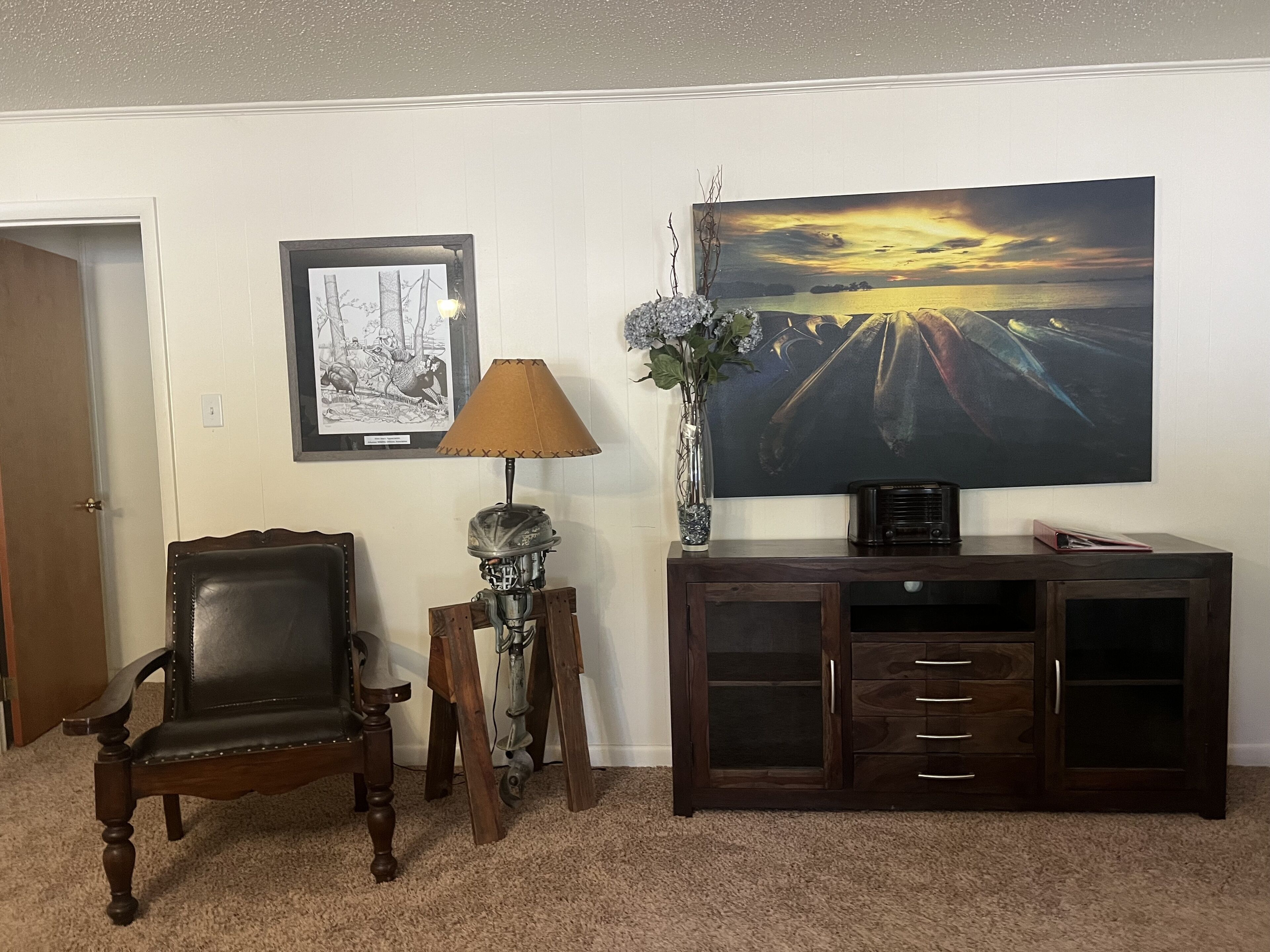 Una sala de estar con un televisor de pantalla plana grande, una silla de madera, una lámpara y un aparador.