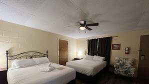 Ein Hotelzimmer mit zwei Betten, einem Deckenventilator, einem Sessel und einer Tür.