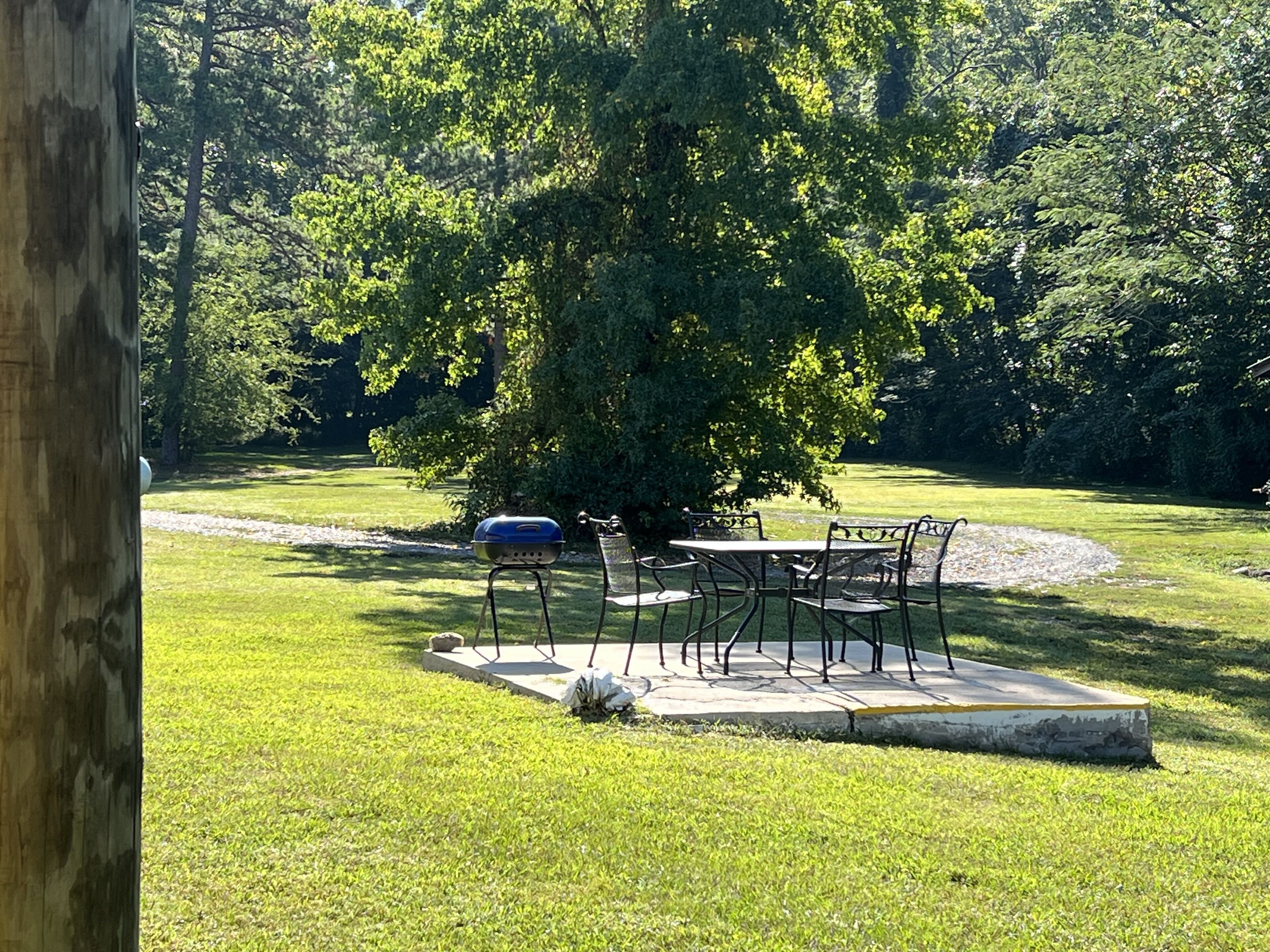 A grassy outdoor area with a barbecue grill, a table, and chairs.