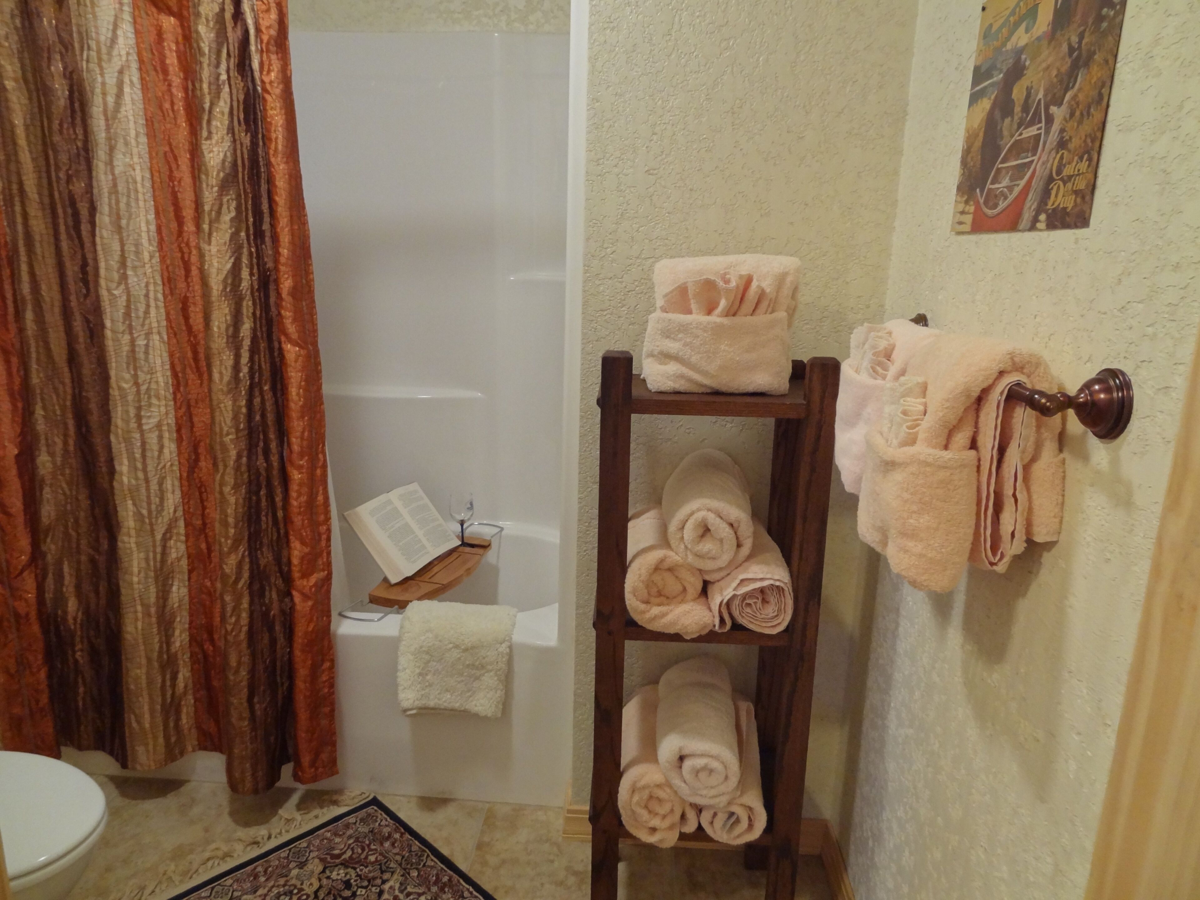Un baño con bañera, un estante de madera con toallas, un perchero y un cuadro en la pared.