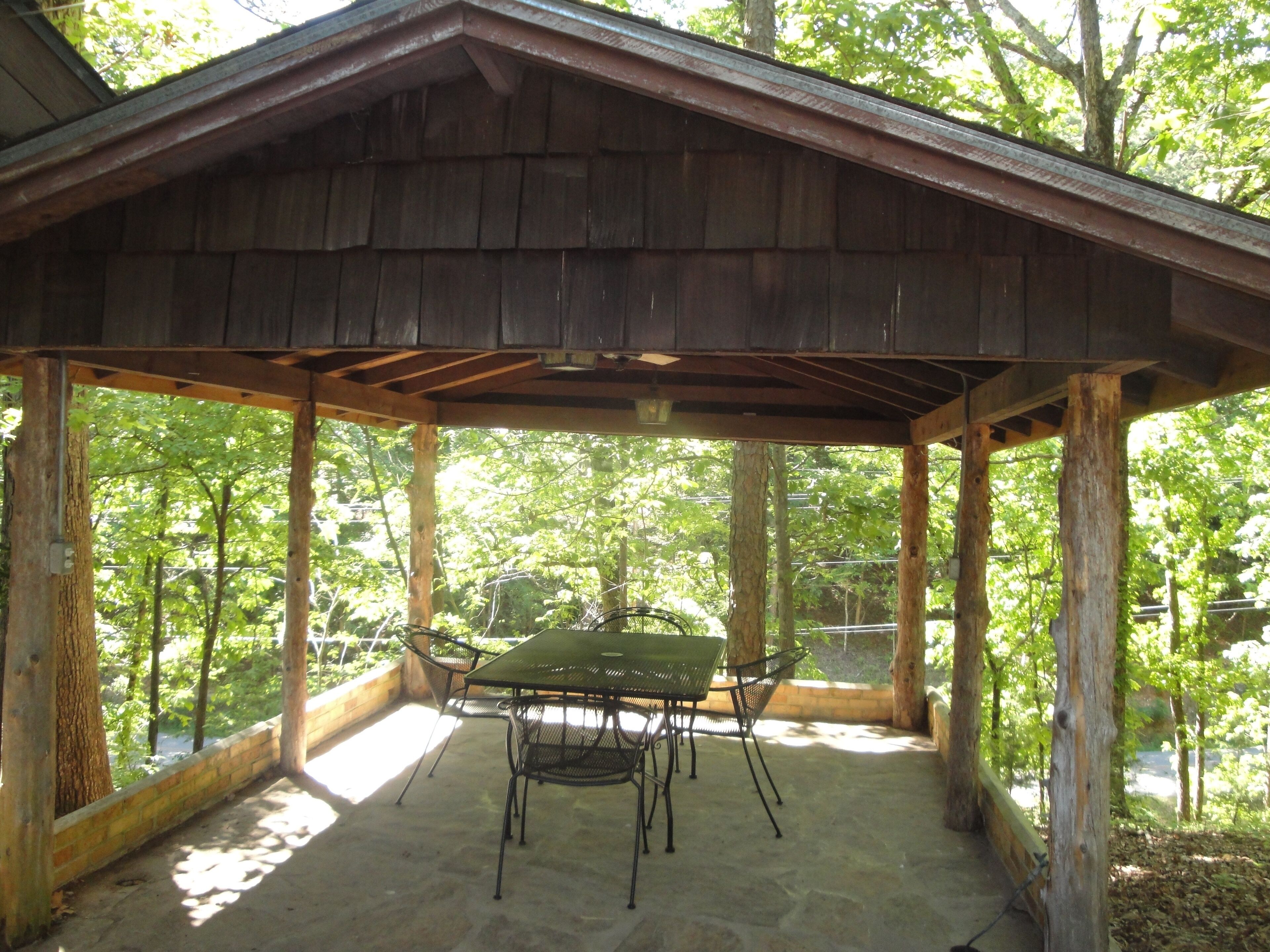 A covered patio with a stone floor, metal table and chairs, and a view of a wooded area.