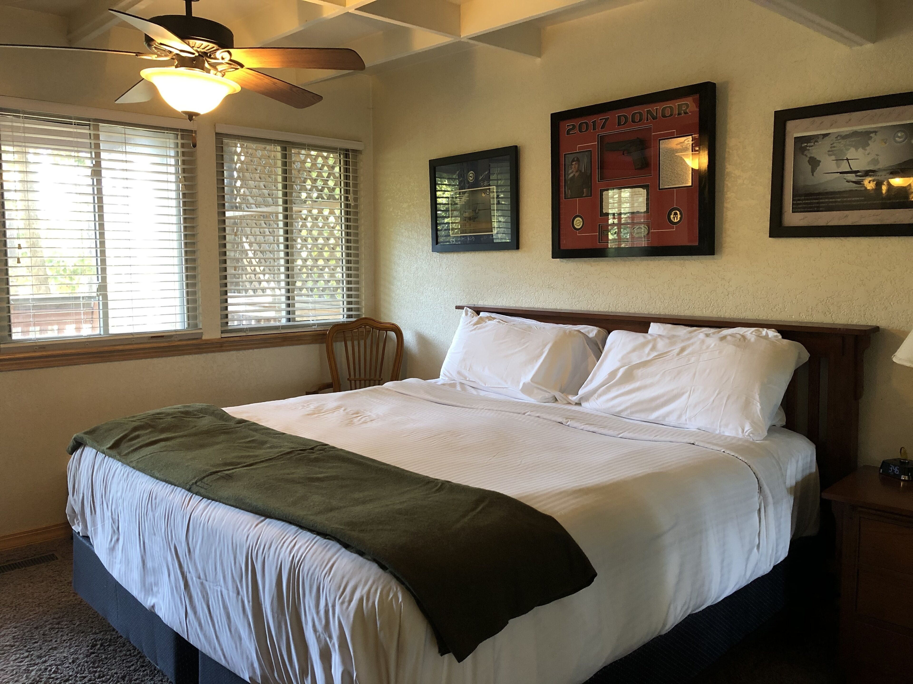 A neatly made bed with white linens and a green throw blanket, a wooden headboard, and a ceiling fan.