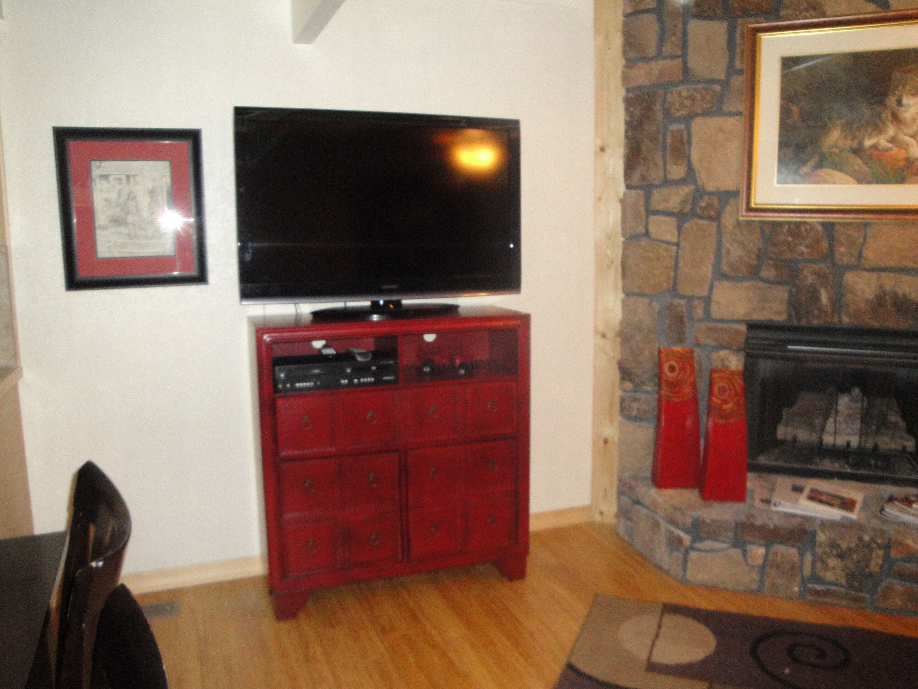 A living room with a television on a wooden cabinet, a fireplace with a stone surround, and a framed picture on the wall.