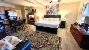 Habitación de hotel con cama, escritorio, silla, televisor y ventilador de techo.