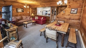 Interior acogedor de una cabaña con una mesa de comedor de madera, un sofá rojo y una cocina visible a través de una puerta abierta.