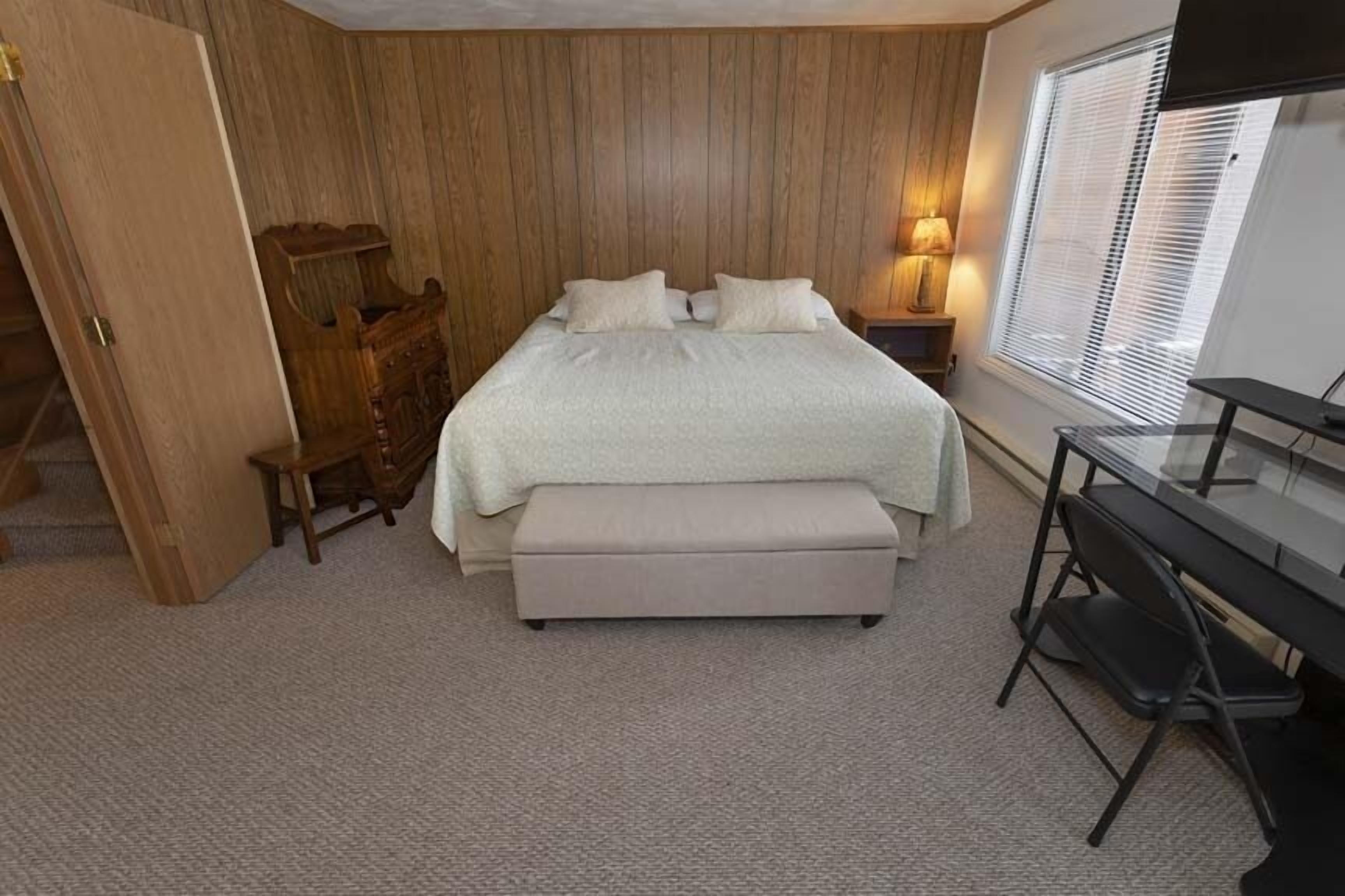 A bedroom with a bed, a bench, a desk, and a lamp.