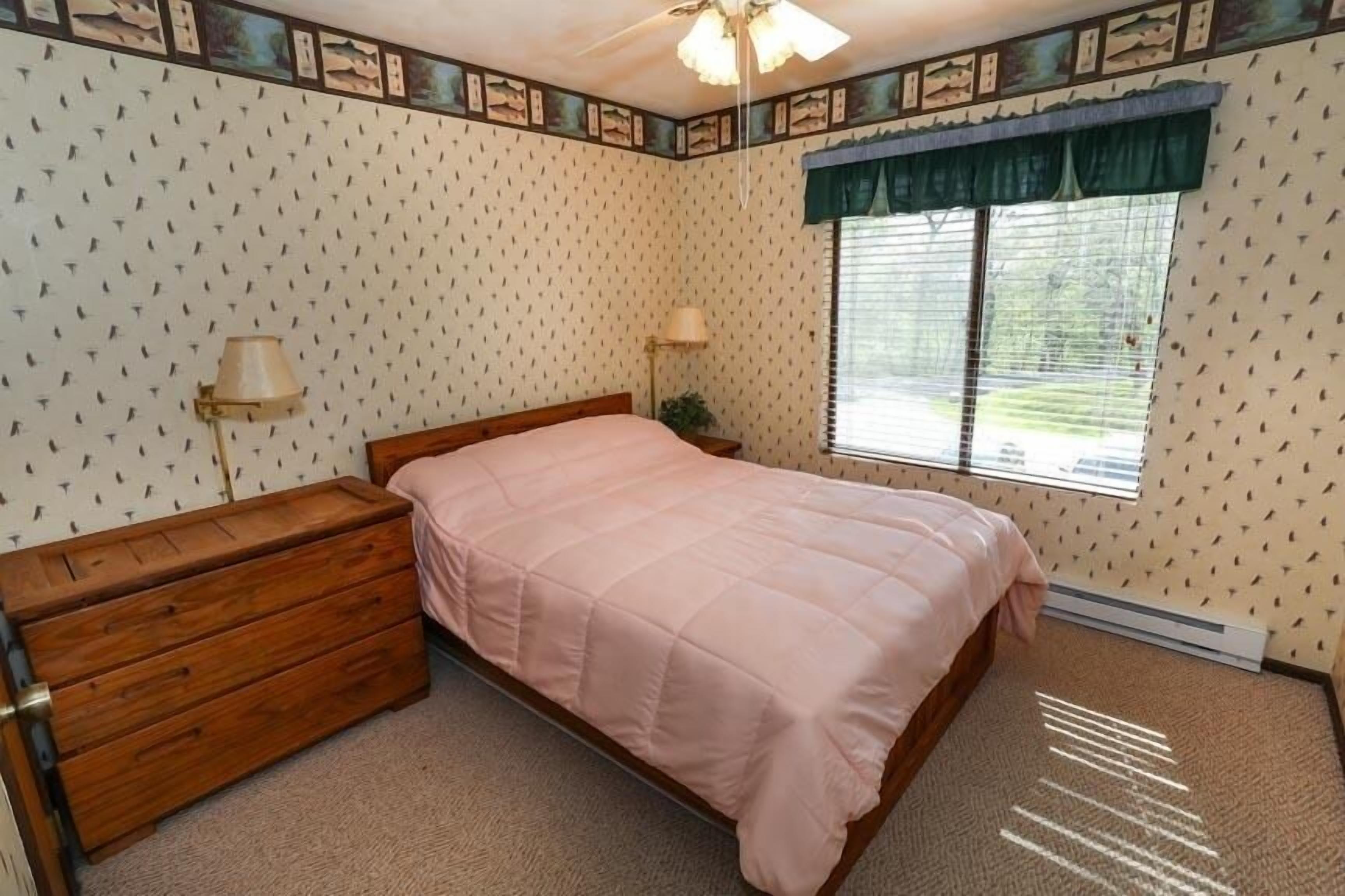 Quarto com cama, cômoda, luminária e janela com persianas.