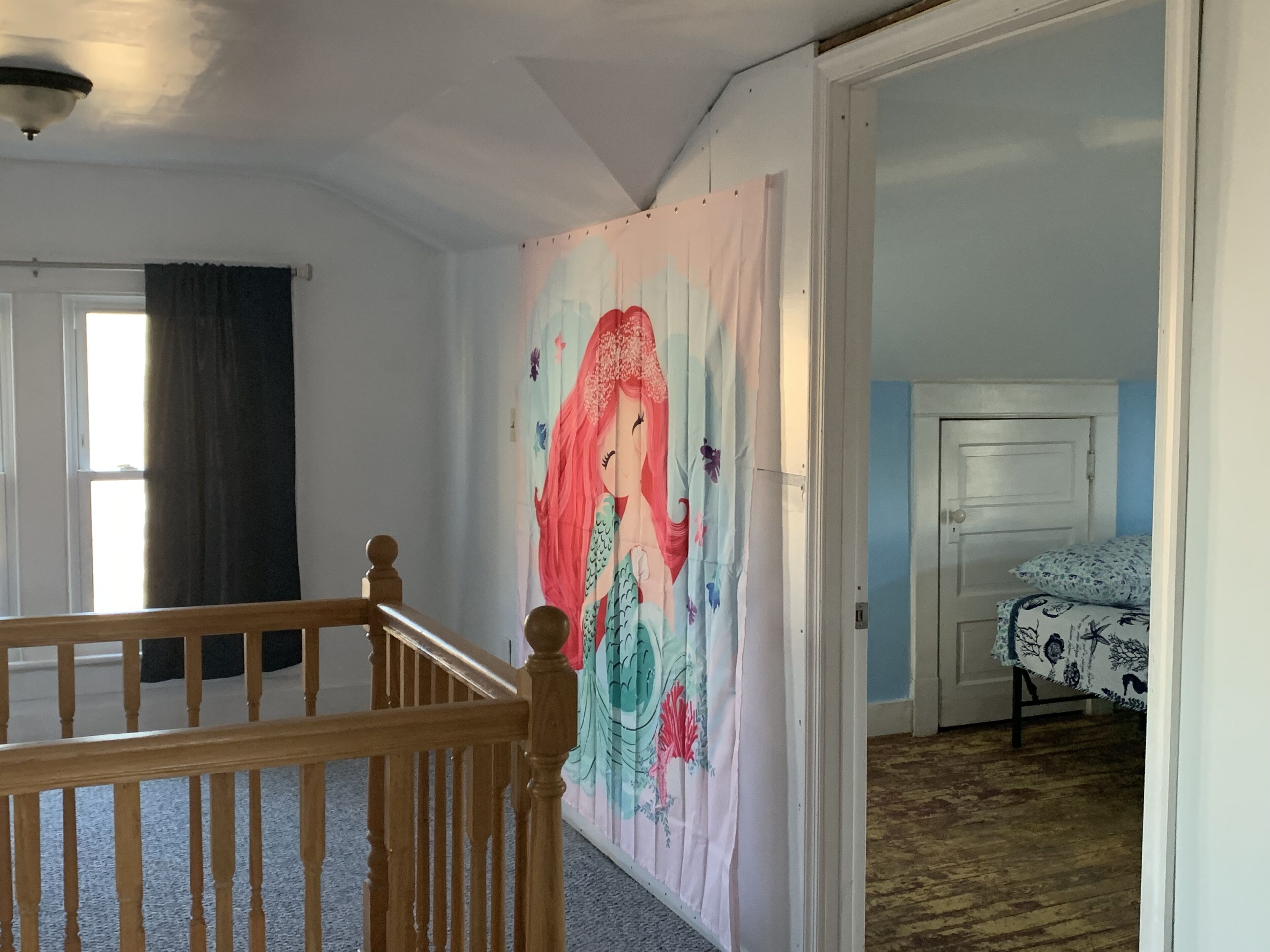 A room with a wooden staircase, a large mural on the wall, a bed with patterned bedding, and a door leading to another room.