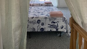 A bedroom with two beds, a wooden headboard, a large window with sheer curtains, and a chandelier. - Mermaids & Mutts 3 Bedroom Bungalow by RedAwning (Norfolk)