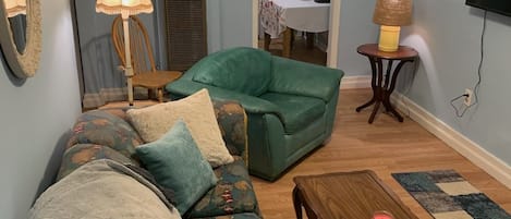 A living room with a green sofa, a wooden coffee table, and a TV mounted on the wall.