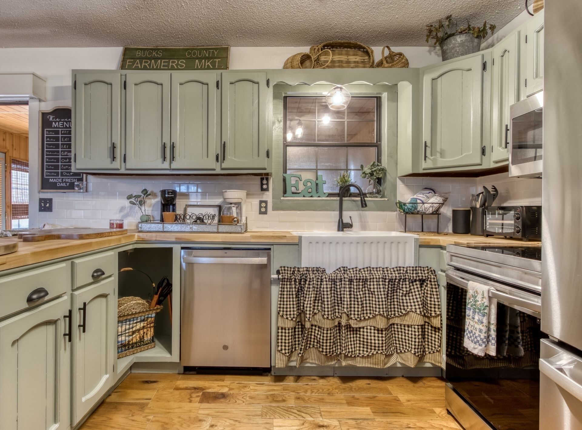 A kitchen with light green cabinets, a window with a hanging light, a dishwasher, and a stove.
