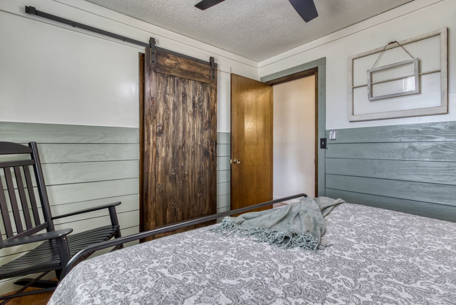 A bedroom with a bed, a wooden wardrobe, a bench, and a wall-mounted picture frame.