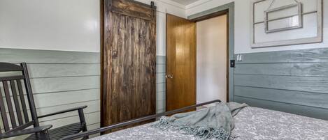 A bedroom with a bed, a wooden wardrobe, a bench, and a wall-mounted picture frame.