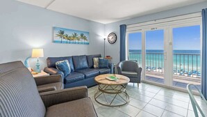Ein Wohnzimmer mit blauem Sofa, rundem Couchtisch und Blick auf den Strand durch große Fenster.
