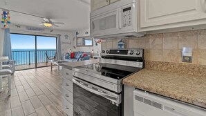 Eine moderne Küche mit Edelstahlgeräten, einem großen Backofen und einer Mikrowelle. Es gibt einen Balkon mit Blick auf das Meer.