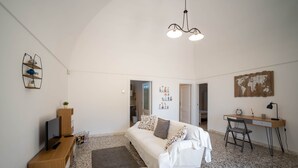 Uma sala de estar moderna com um sofá branco, um móvel para TV de madeira, uma mesa de centro redonda, uma escrivaninha com uma cadeira e um mapa-múndi na parede.