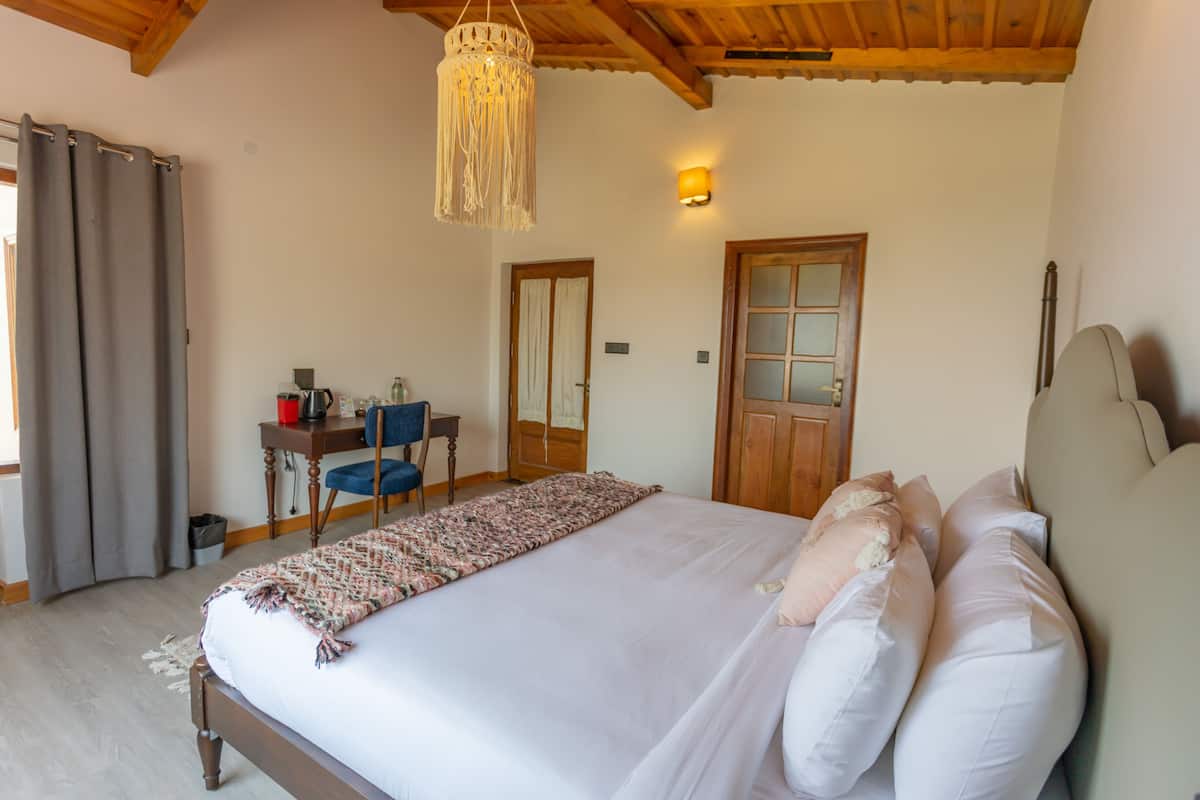 A bedroom with a large bed, a desk with a chair, a wooden ceiling, and a door.