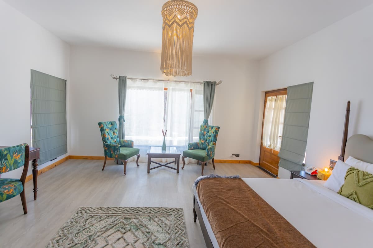 A bedroom with a bed, two chairs, a small table, and a hanging light fixture.