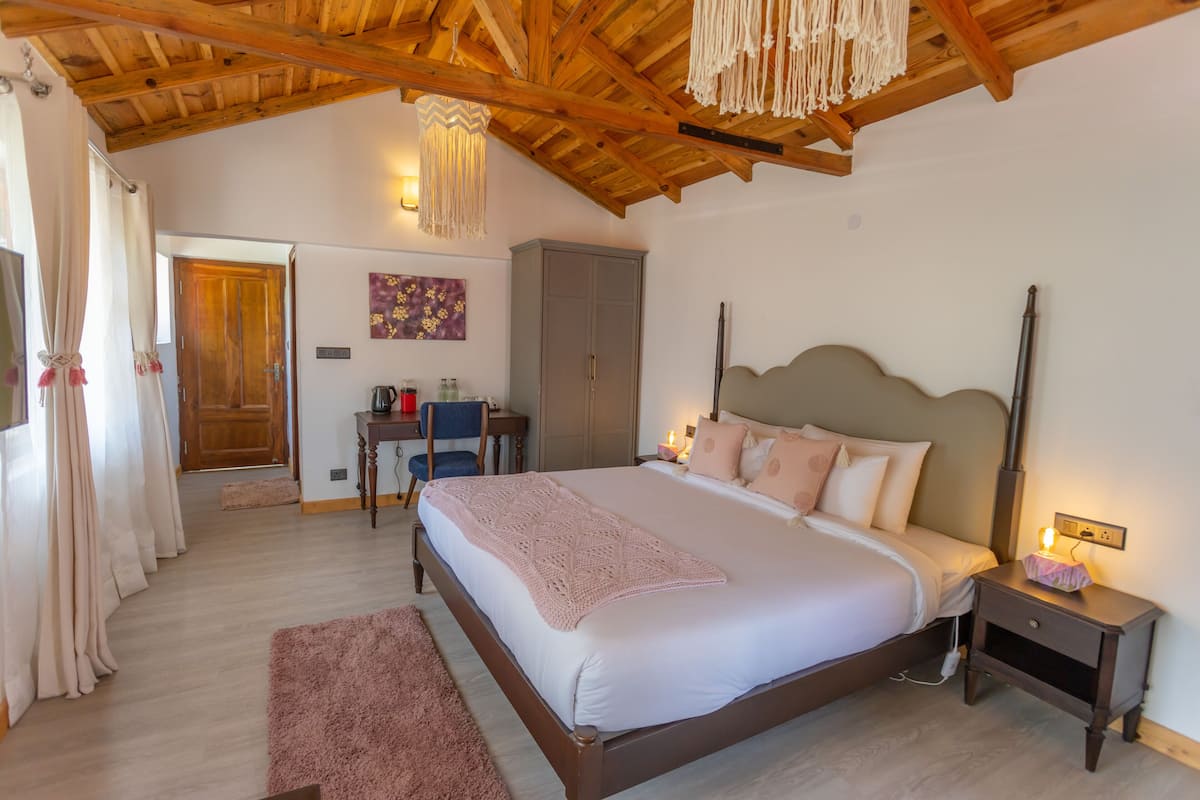 A bedroom with a wooden ceiling, a bed with a headboard, a nightstand, a desk, and a wardrobe.