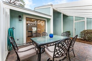An outdoor patio with a glass table and metal chairs, a blue vase, and a hose on the left. - Beach Villa w/ 4-Seat GOLF CART! Near Beach & Pool. Screened Porch, Yard (Miramar Beach)