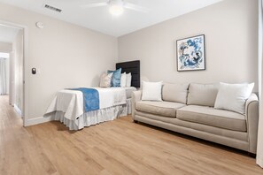 A modern living room with a bed, a sofa, and a ceiling fan. - Beach Villa w/ 4-Seat GOLF CART! Near Beach & Pool. Screened Porch, Yard (Miramar Beach)