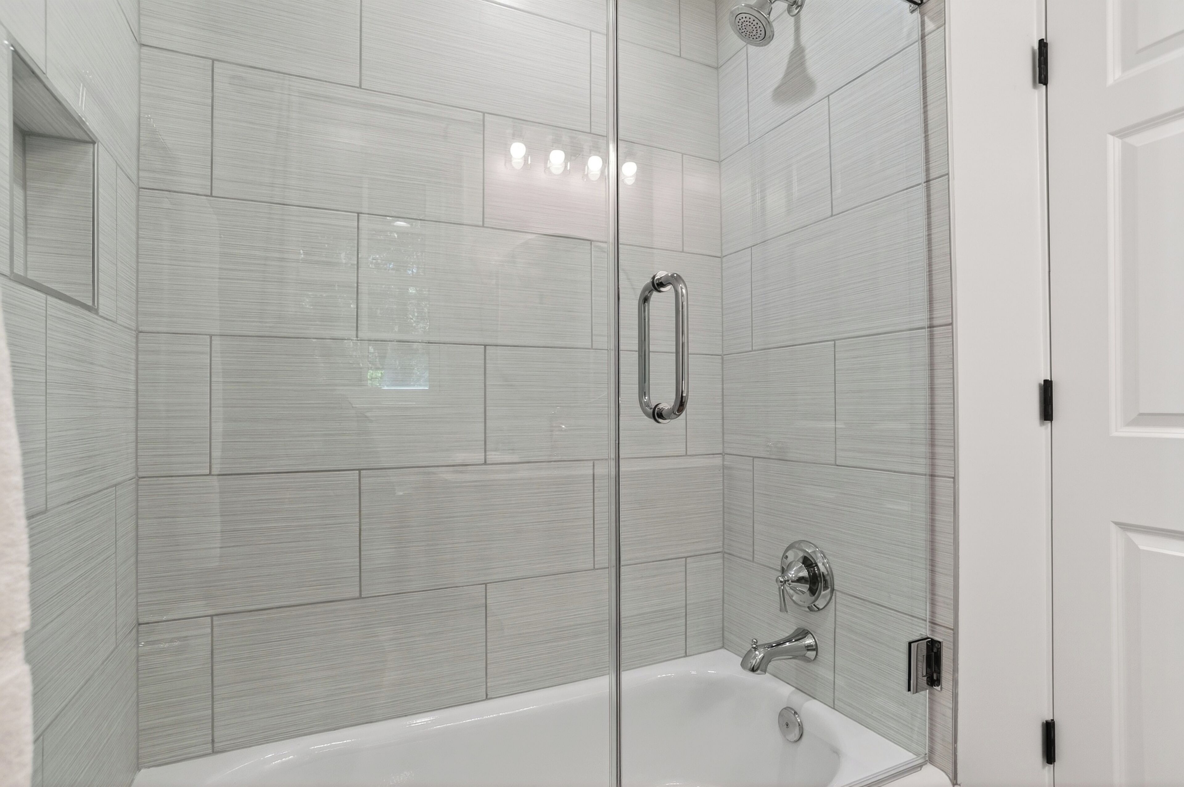 Ein modernes Badezimmer mit einer Glaskabine zur Dusche, weißen Fliesen und einer weißen Badewanne.