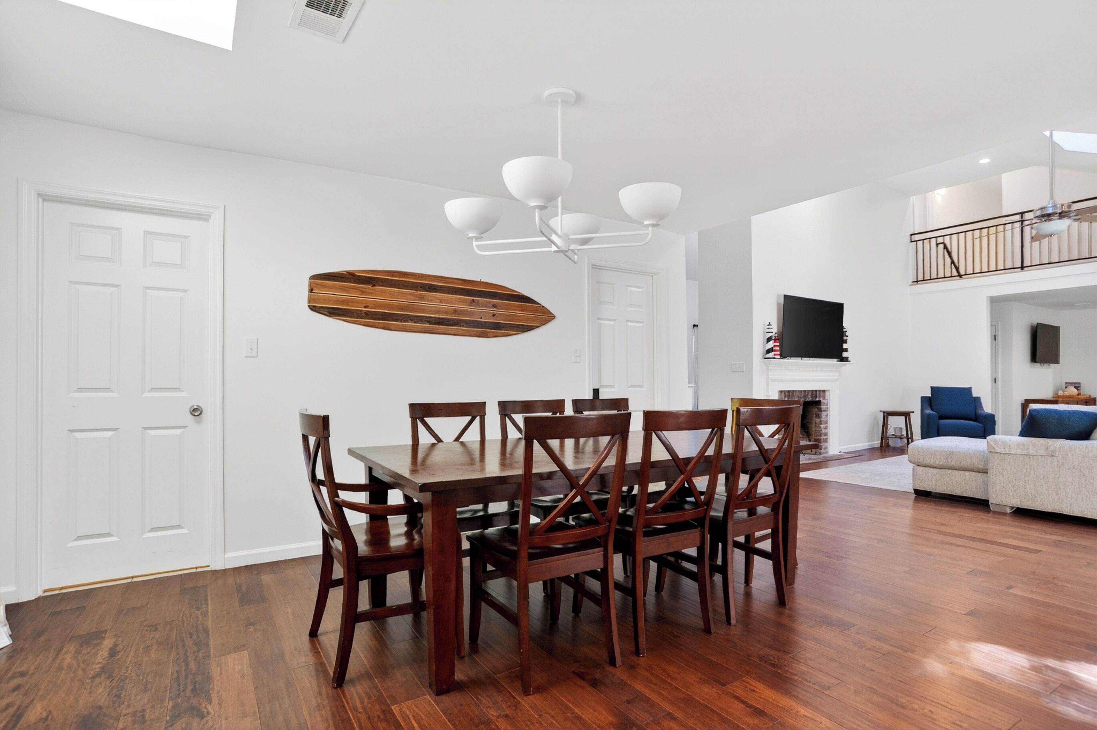 A dining area with a wooden table and chairs, a chandelier, and a television in the background.
