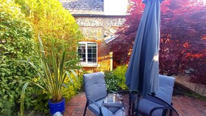 A patio with a round glass table and two chairs, a potted plant, and a house with a tiled roof in the background. - Beautiful, traditional rural cottage (Shrewton)