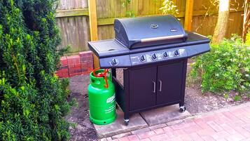A black barbecue grill with a gas tank beside it.