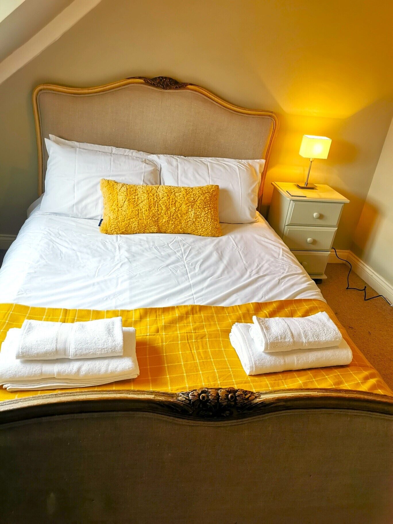 A neatly made bed with white linens, a yellow throw blanket, and two folded towels.