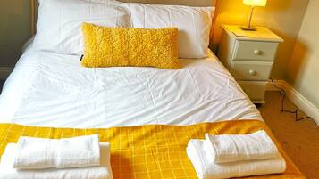 A neatly made bed with white linens, a yellow throw blanket, and two folded towels.