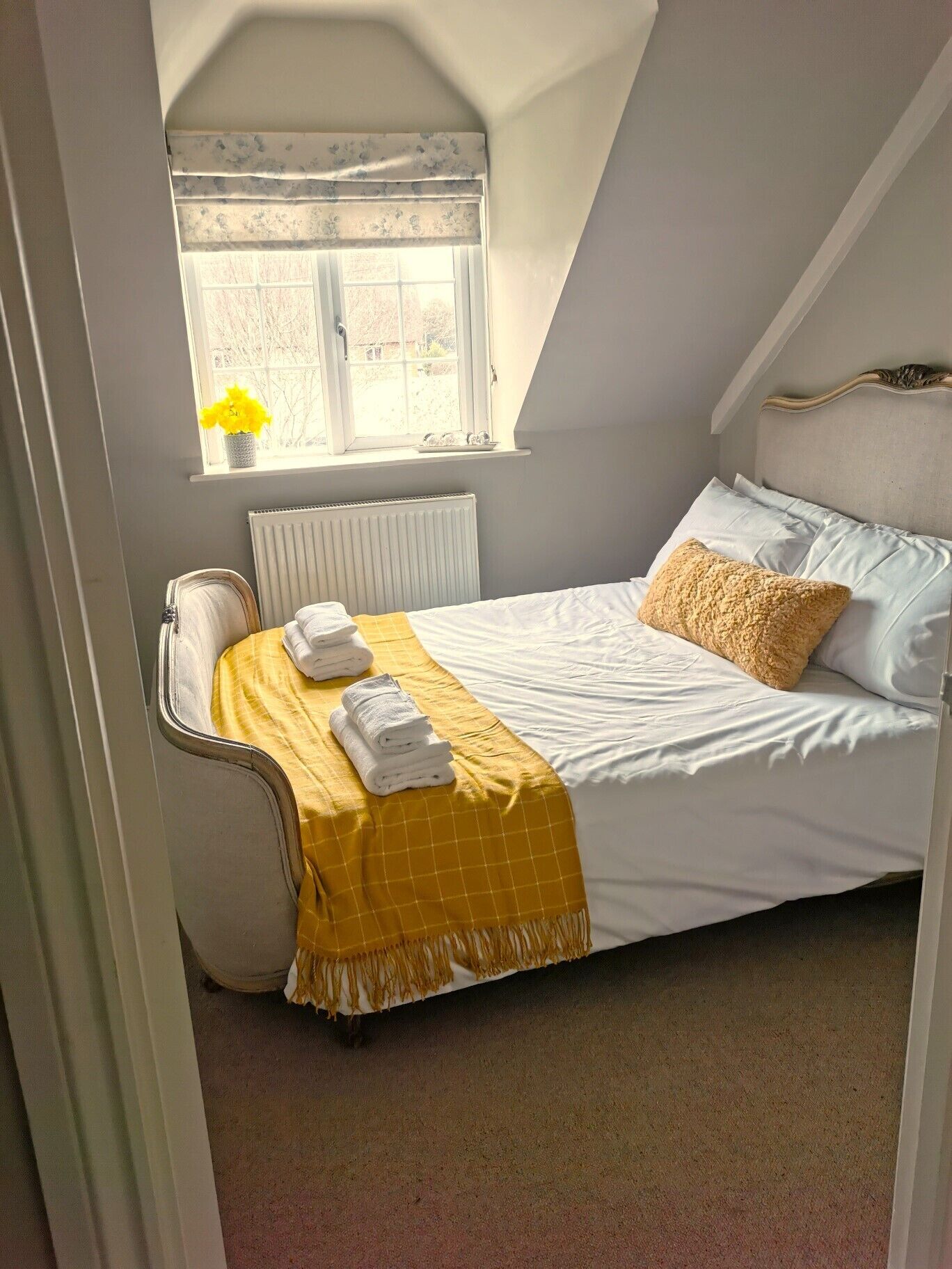 A bedroom with a bed, a window with a view, a radiator, and a yellow throw blanket.