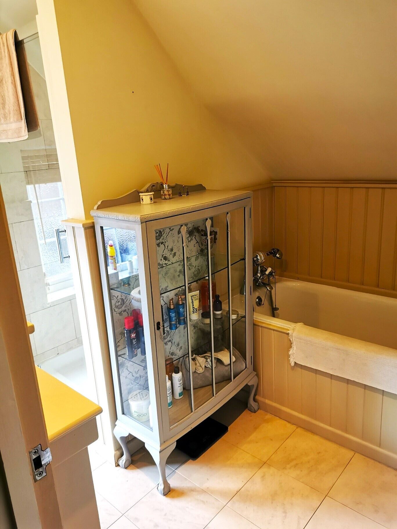 A bathroom with a glass-fronted cabinet, a bathtub, and a yellow wall.
