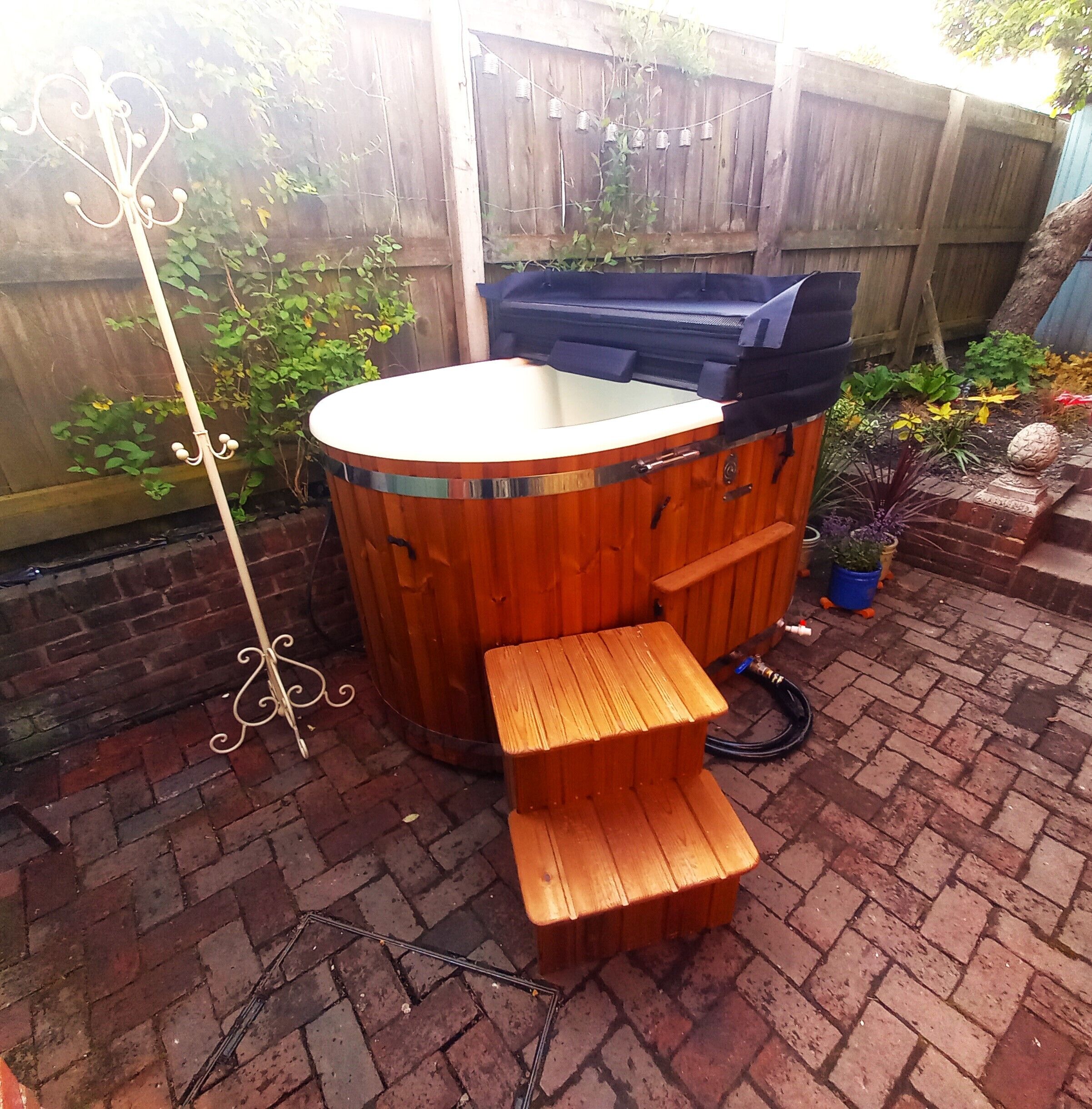 A wooden hot tub with a bench, surrounded by a brick patio and a wooden fence.
