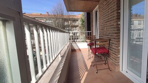 Ein Balkon mit weißer Brüstung, einem roten Stuhl und einem Tisch.