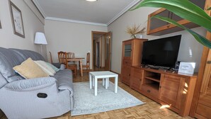 Ein Wohnzimmer mit grauem Sofa, einem weißen Couchtisch, einer Holzkassette mit Fernseher und Holzboden.